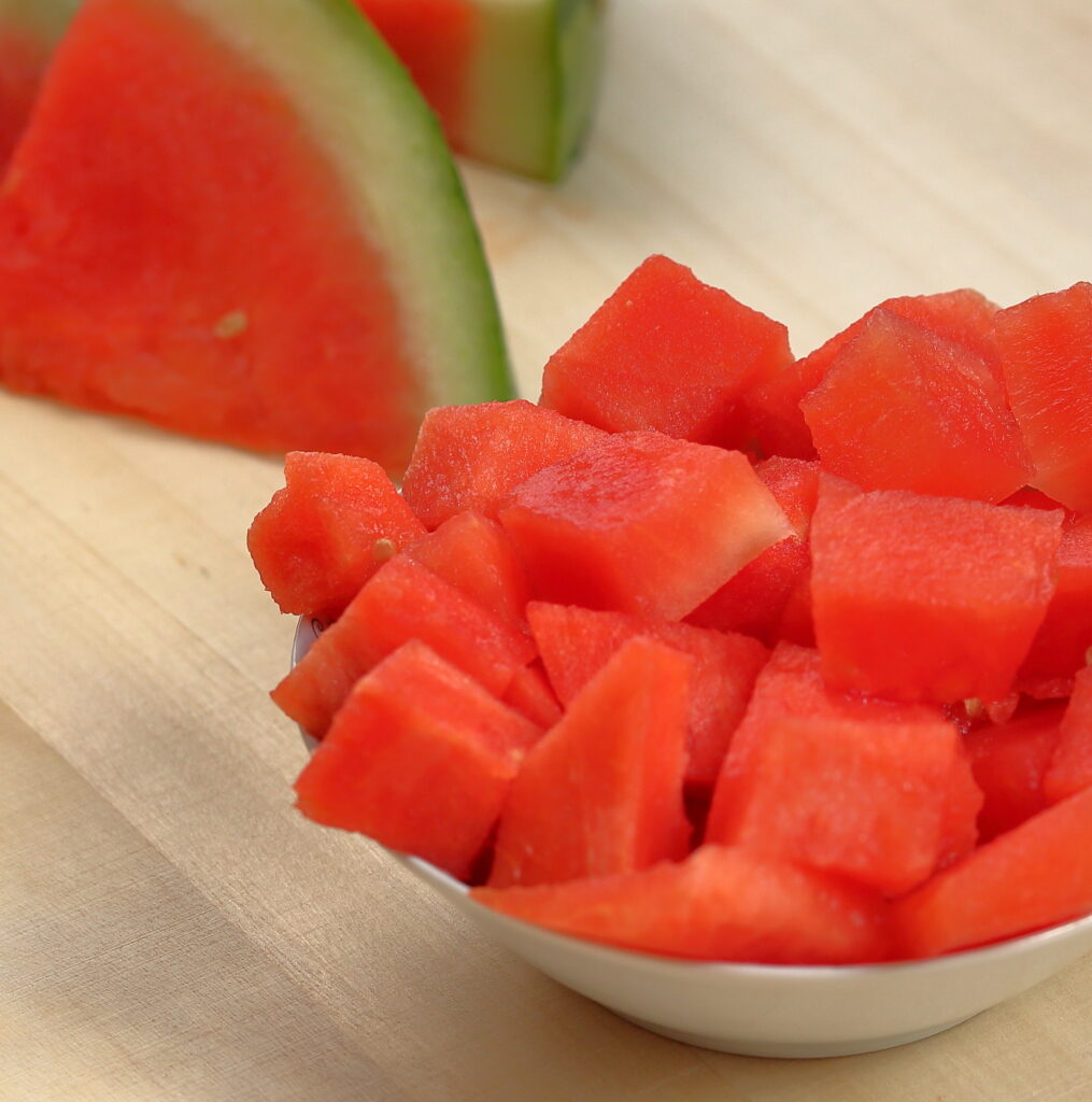 fresh watermelon cut in pieces in a bowl and in slices on wooden table close up By Wioletta
