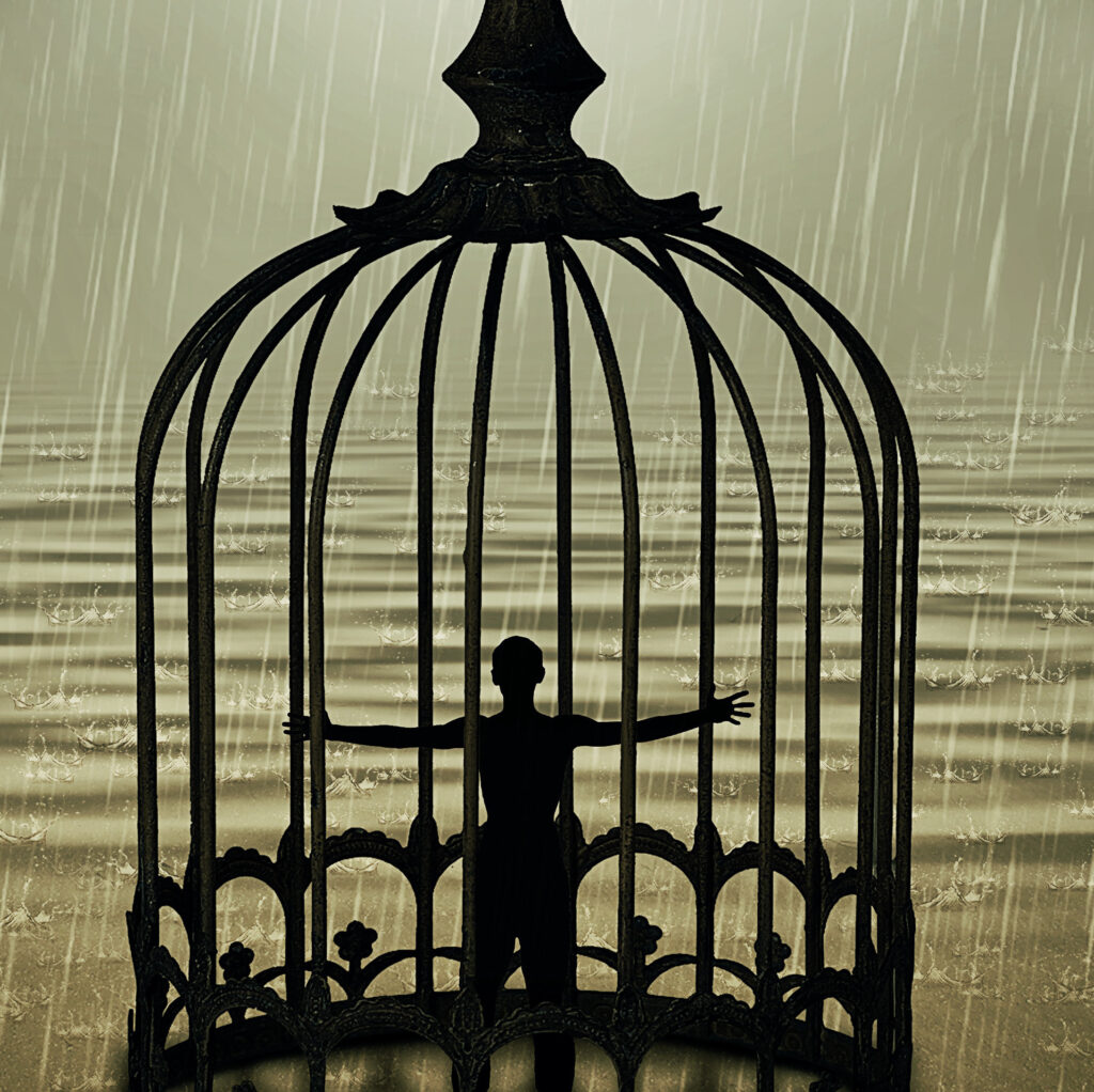 Man standing closed in a bird cage with wide opened hands in front of the ocean horizon in a rainy day. Life limitation, trapped in a prison concept By psychoshadow