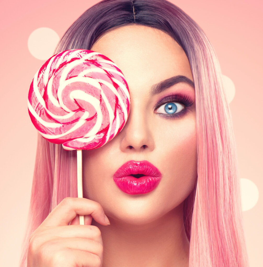 Beauty sexy model woman with trendy pink hairstyle and beautiful makeup holding lollipop candy, on pink polka dots background By Subbotina Anna